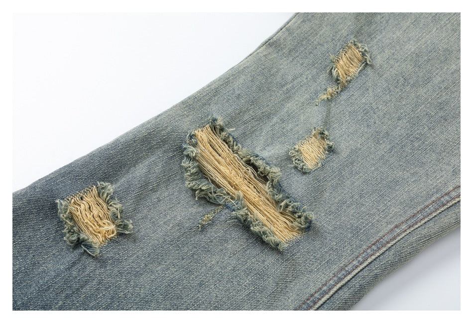 Close-up of faded blue denim with several frayed distressed patches and tan threads.
