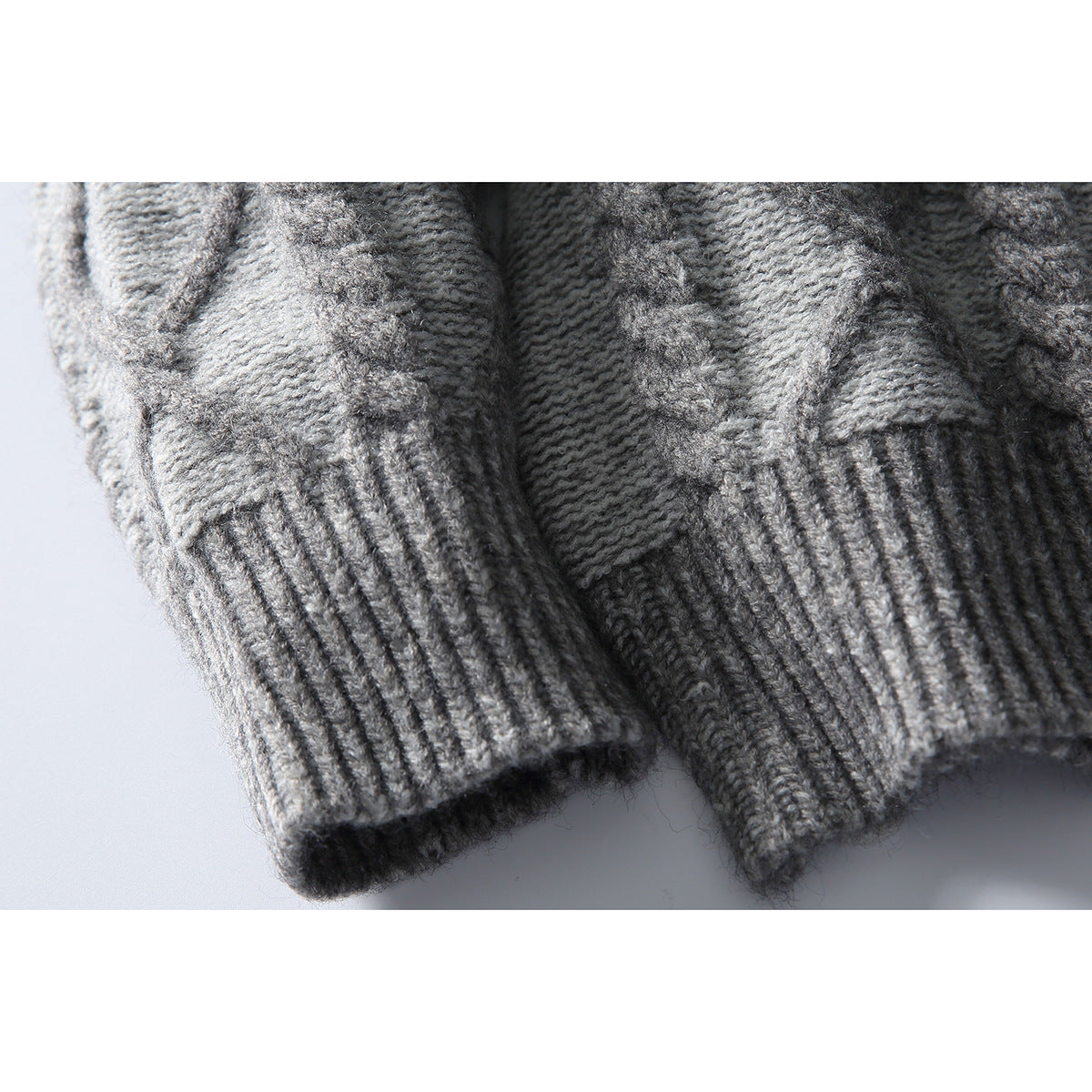 Close-up of gray cable-knit sweater sleeves and ribbed cuffs.