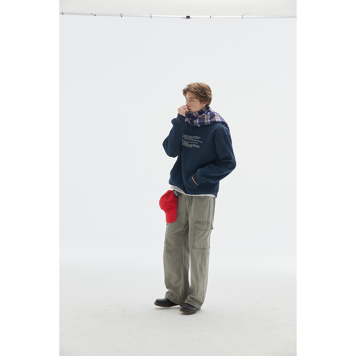 Model wearing a navy hoodie with small white chest text, plaid scarf, and gray cargo pants.