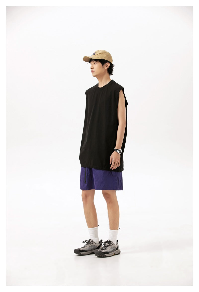 Model in profile wearing a black sleeveless shirt, purple shorts, a tan cap, and hiking shoes.