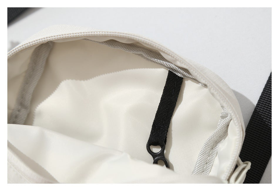 Close-up of a white bag's interior, showing the lining, stitched edge, and a black strap with a clip.