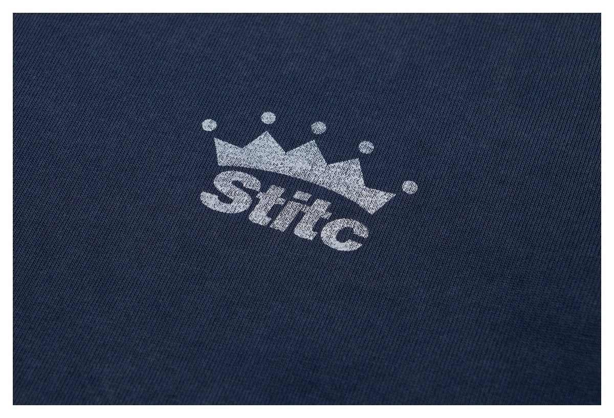 Close-up of a white crown and “Stilc” print on dark navy ribbed fabric.