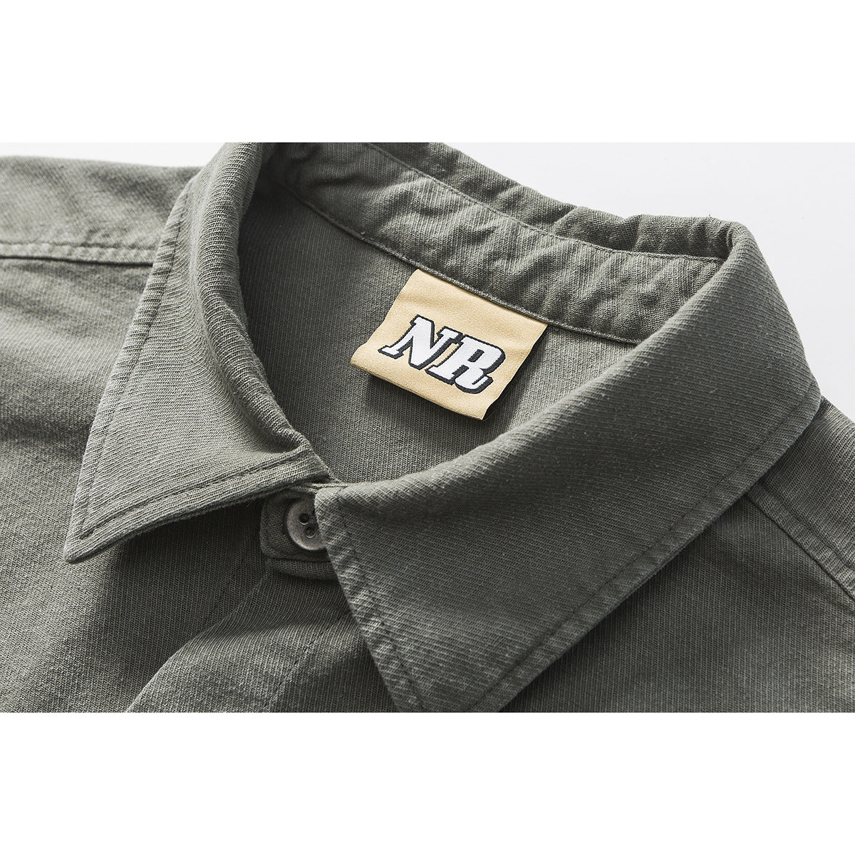 Close-up of a charcoal gray shirt collar, button, and beige neck label with an NR logo.