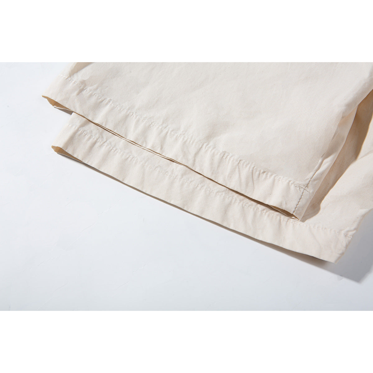 Close-up of the off-white shirt's double-stitched hem and overlapping fabric edge.