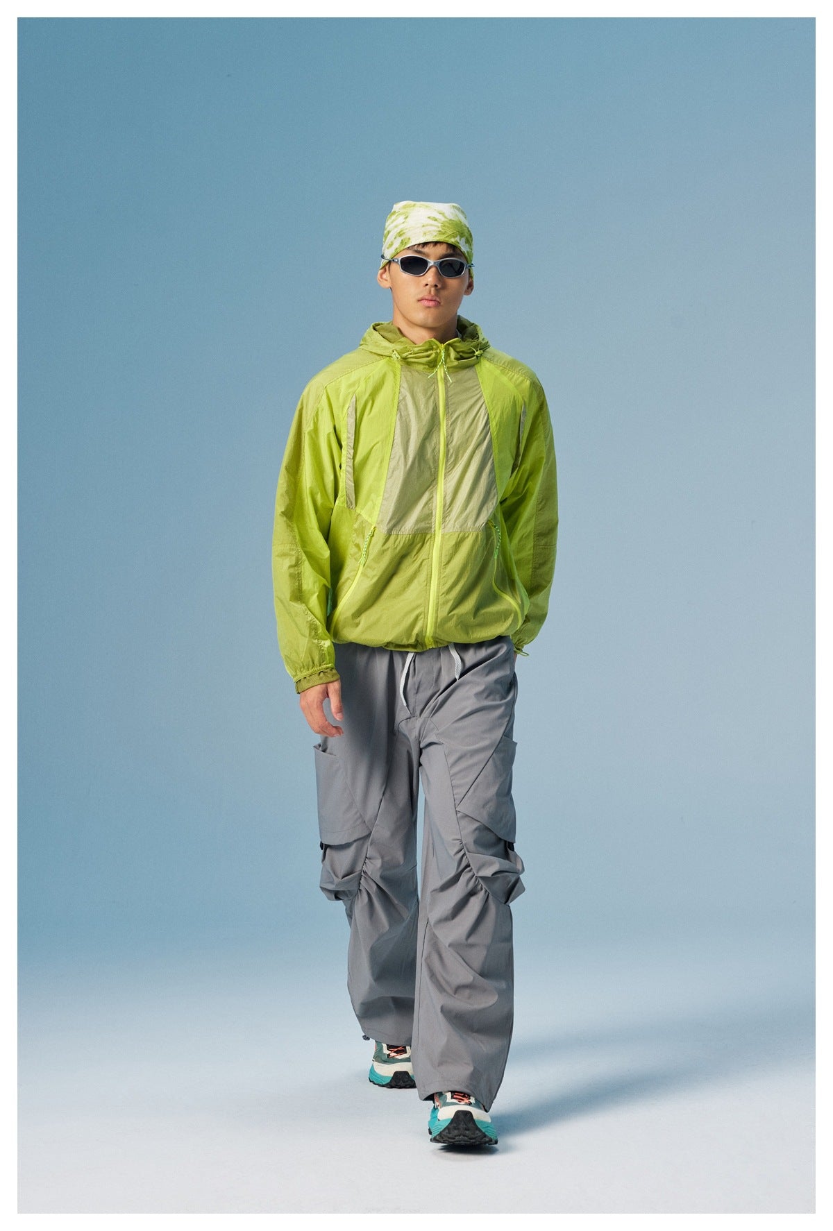 Man models a lime green color-block hooded jacket with gray cargo pants while walking toward the camera.