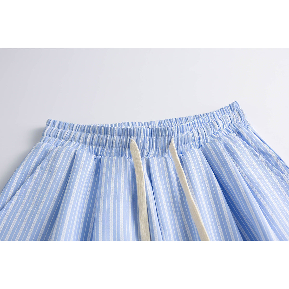 Close-up of light blue and white striped shorts with an elastic waistband and cream drawstrings.