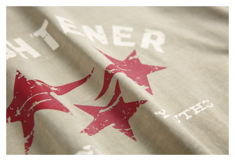 Angled close-up of the T-shirt's distressed red star print and white lettering on sand-beige fabric.