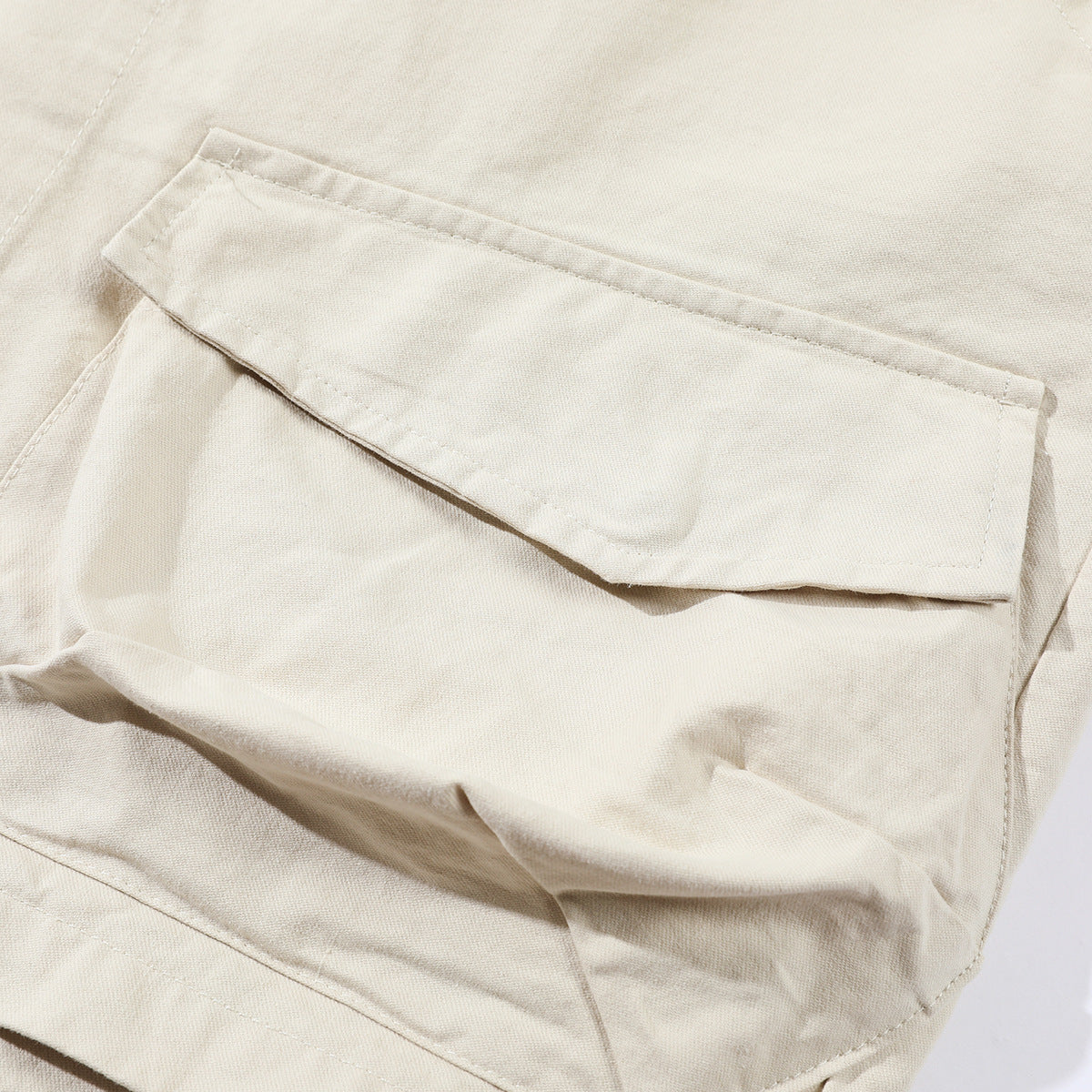Close-up of an off-white jacket pocket flap and surrounding seams.