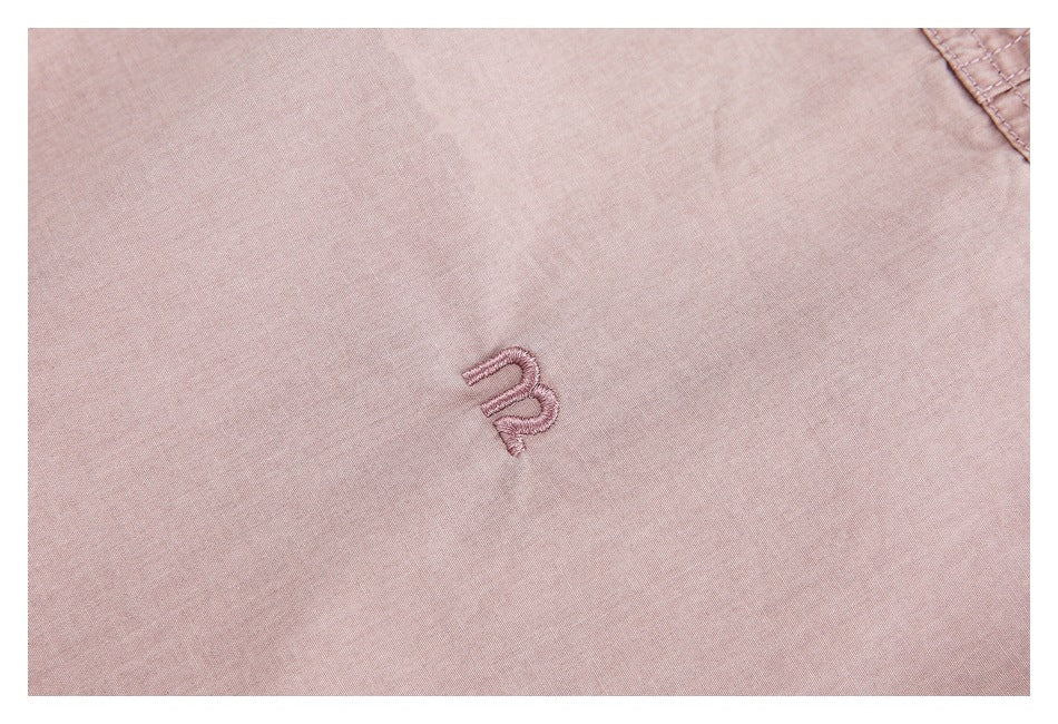 Close-up of a small embroidered emblem on dusty pink shirt fabric.
