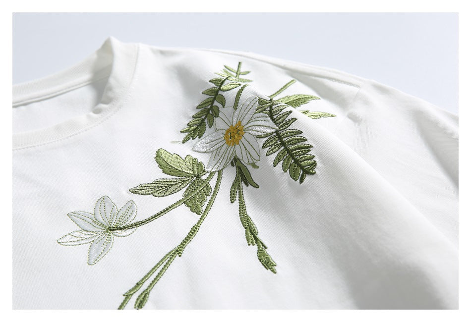 Close-up of a white shirt with embroidered white flowers and green foliage.