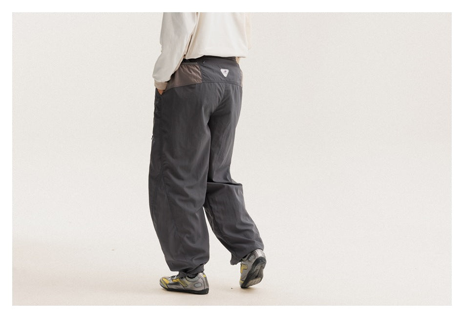 Three-quarter rear view of a model wearing charcoal-gray pants with a contrasting waistband panel.