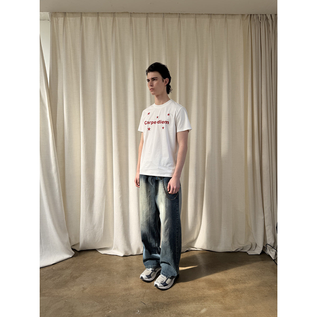 Model wearing a white Carpe diem star-print T-shirt with loose faded jeans, shown full-length.