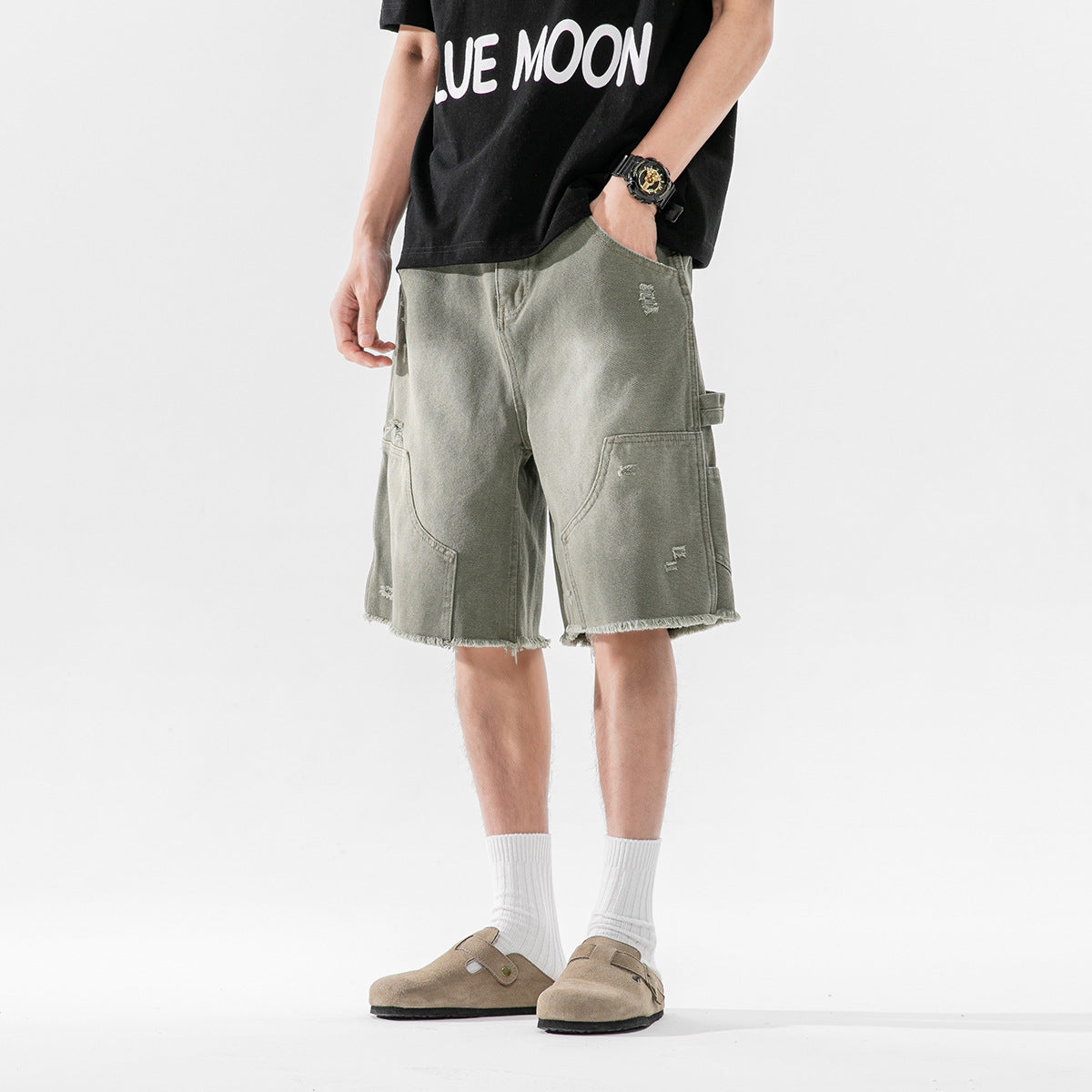 Model wearing olive-gray distressed cargo shorts with large patch pockets and frayed hems, front view.
