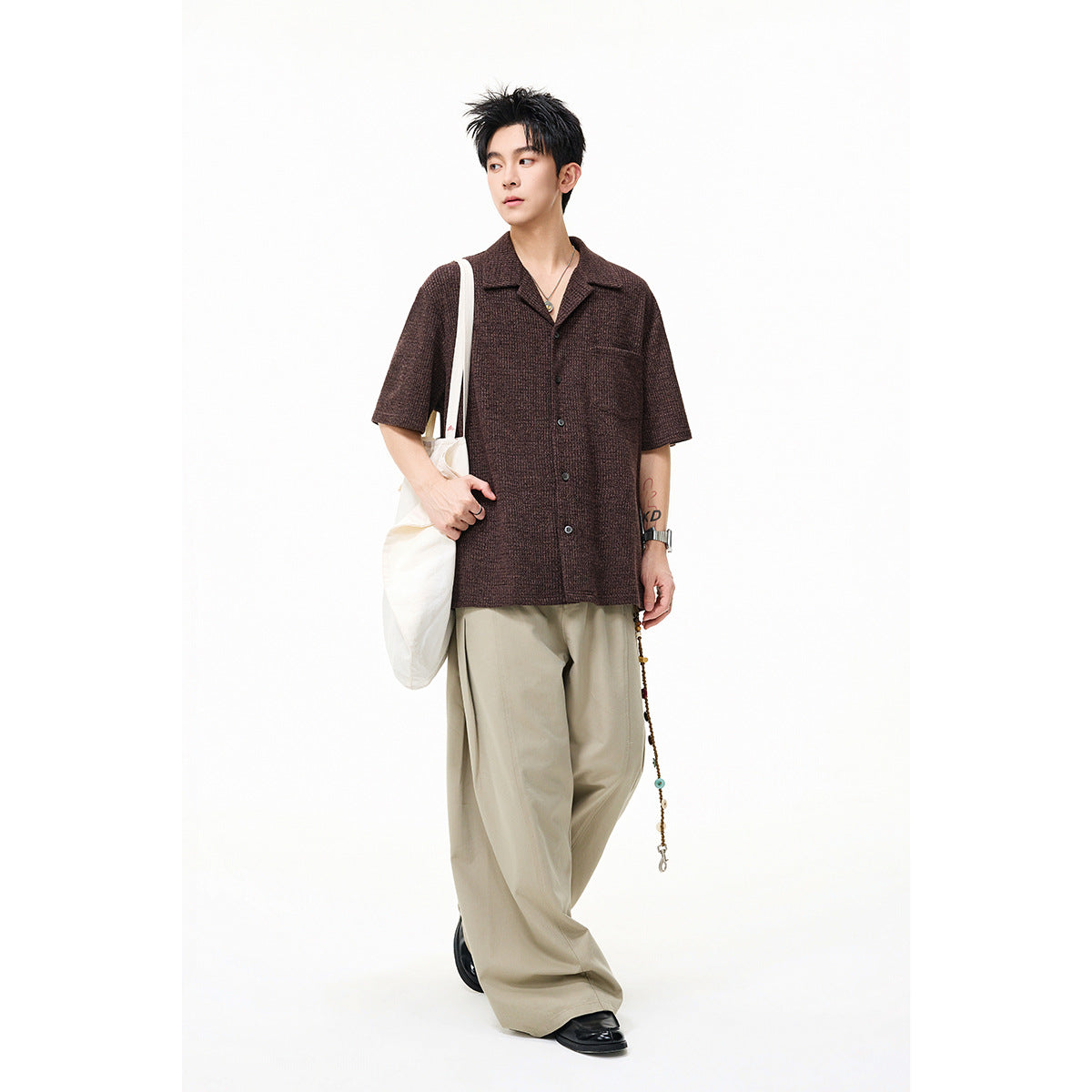 Model wearing a brown short-sleeve button-up shirt with a notched collar and beige wide-leg trousers.
