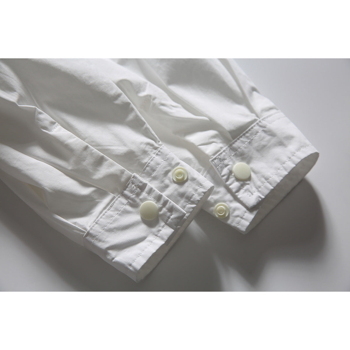 Close-up of the white shirt's sleeve cuffs with snap closures and stitched edges.