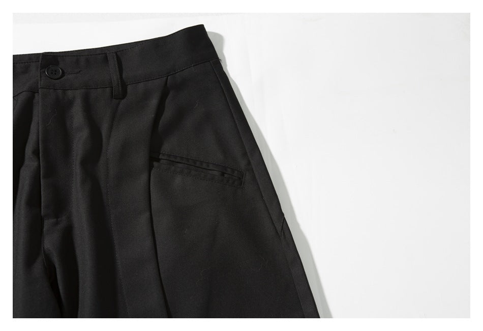 Close-up of black trousers showing the waistband, button, belt loop, pleat, and side pocket opening.
