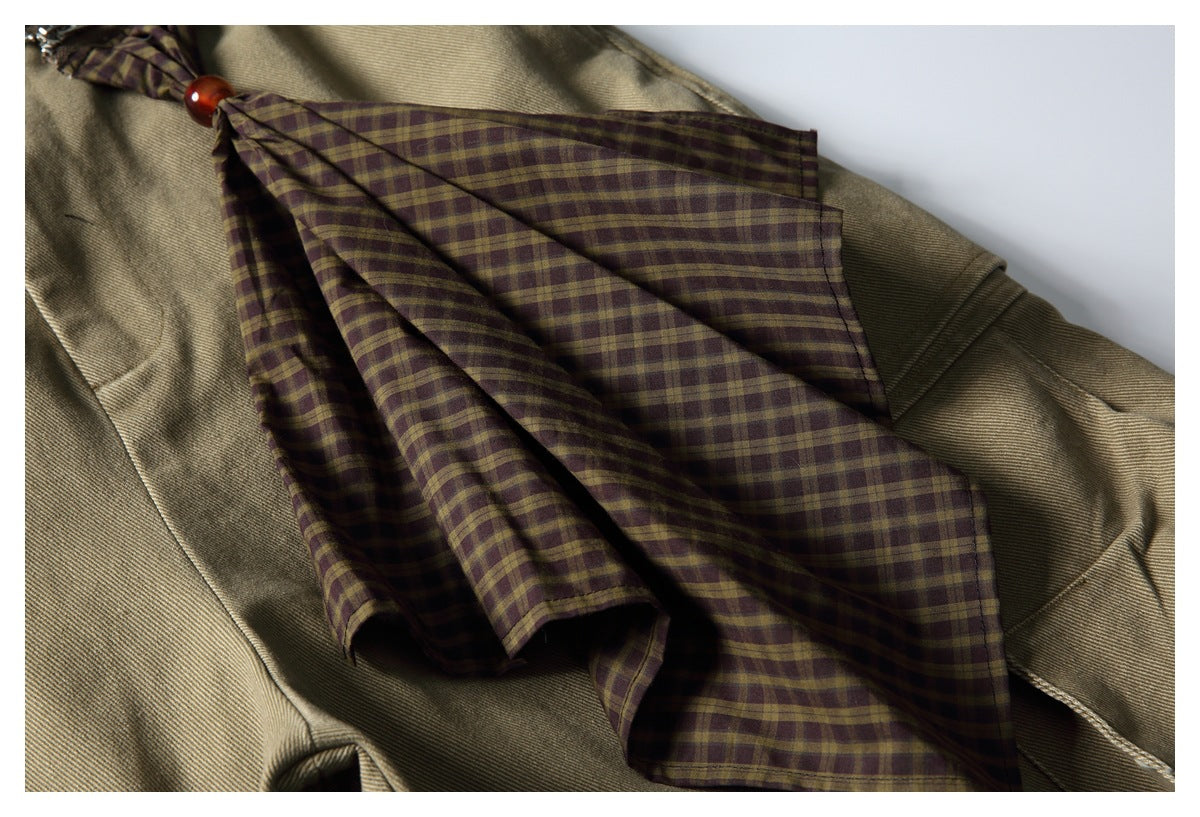 Close-up of a brown and olive plaid lining laid across tan twill fabric, with a small red bead.