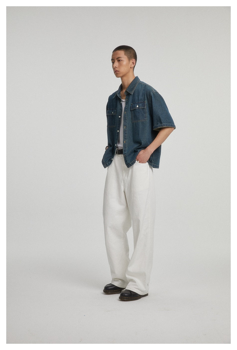 Three-quarter view of a model wearing an open dark blue short-sleeve denim shirt over a white tank and trousers.