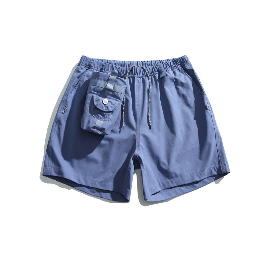 Blue elastic-waist shorts with drawcord, side pockets and a small snap flap pouch at the front, flat lay