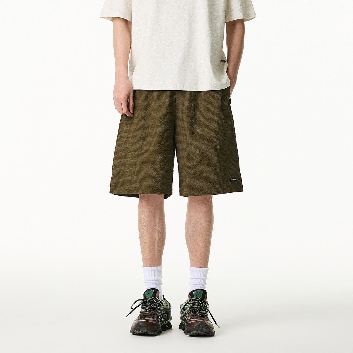 Cropped front view of a model wearing olive textured knee-length shorts with a small hem label.