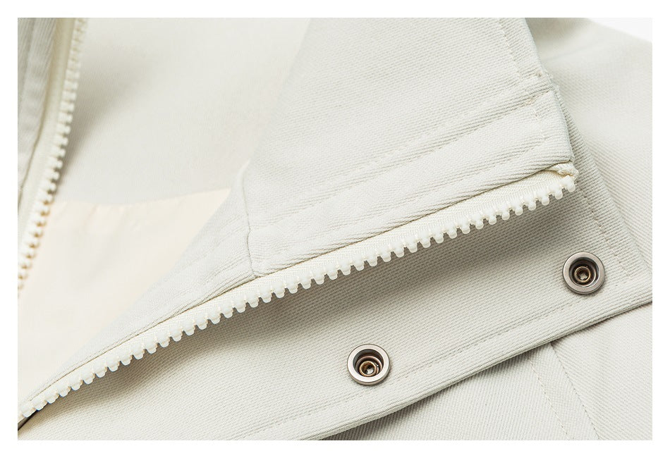 Close-up of an off-white garment's zipper, snap fasteners, and stitched placket.
