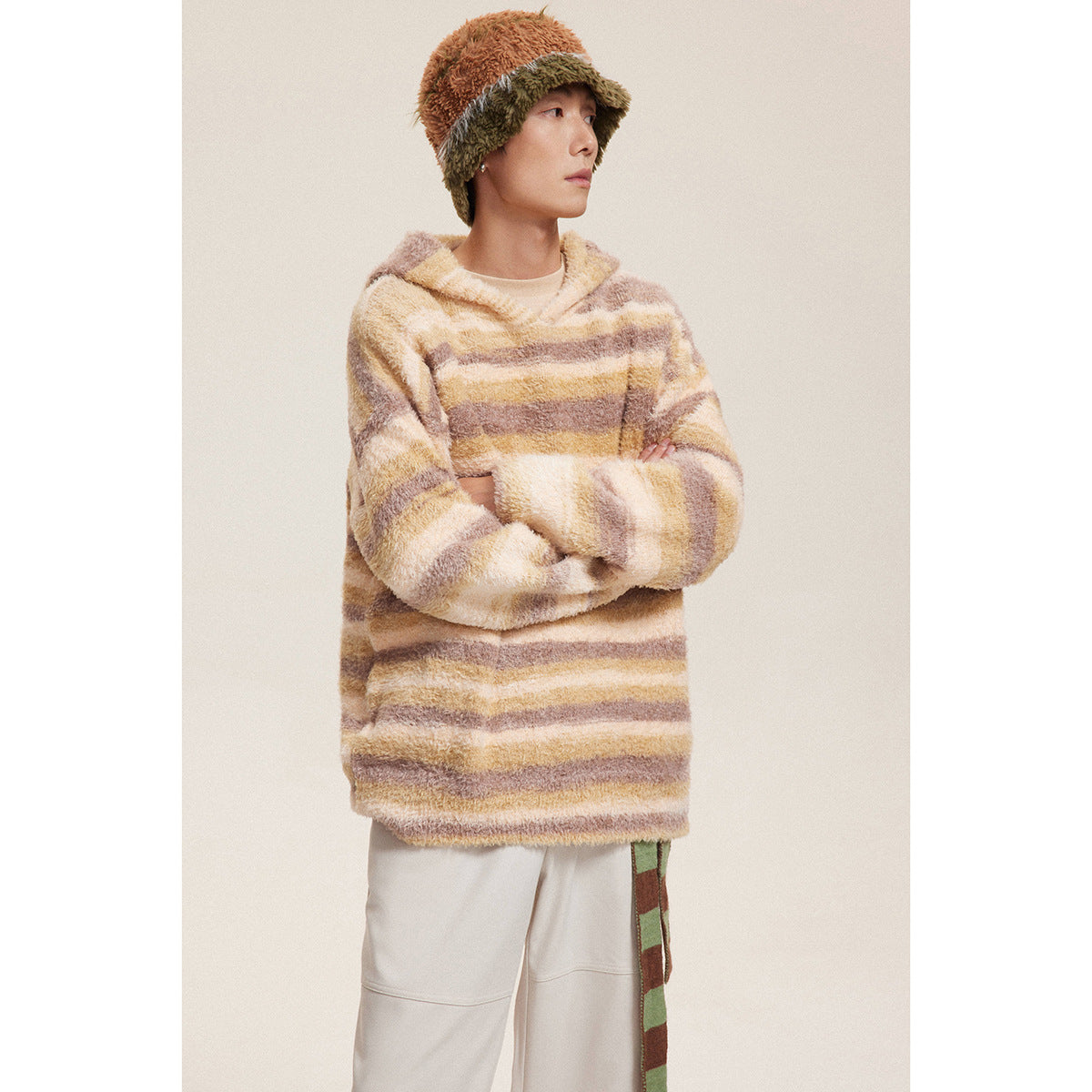 Model wearing a cream, tan, and brown striped hooded sweater with a two-tone fuzzy bucket hat.