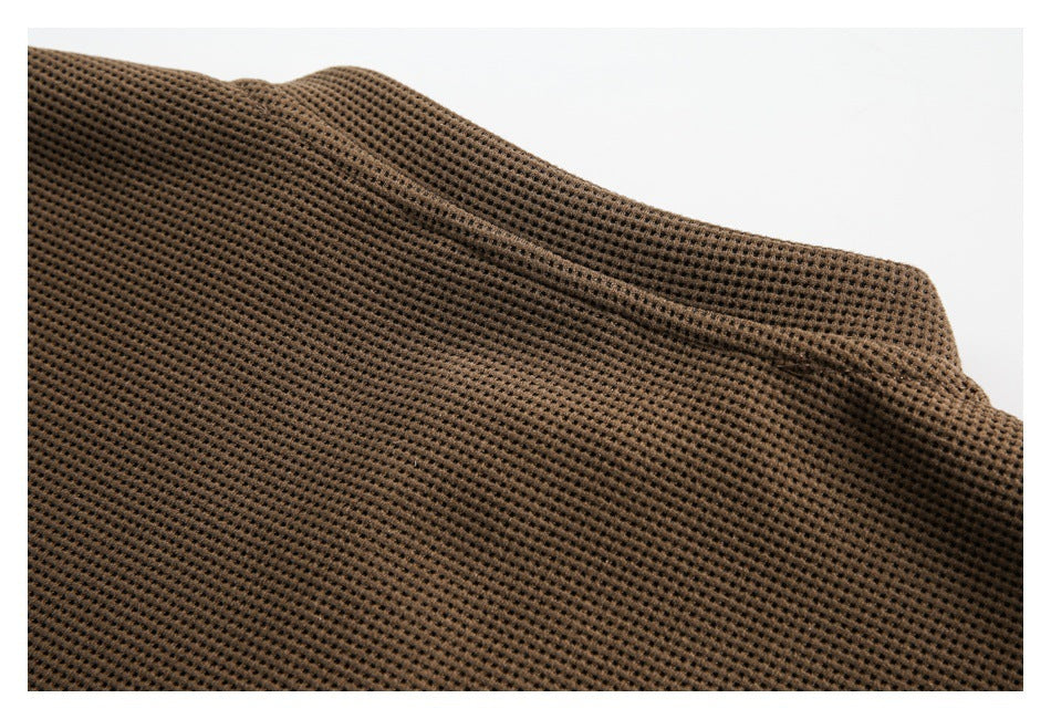 Close-up of brown waffle-knit fabric with a curved seam and folded edge.