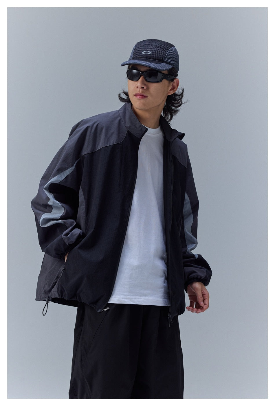 Man wearing a black and charcoal color-block windbreaker with pale sleeve stripes, shown at an angle.