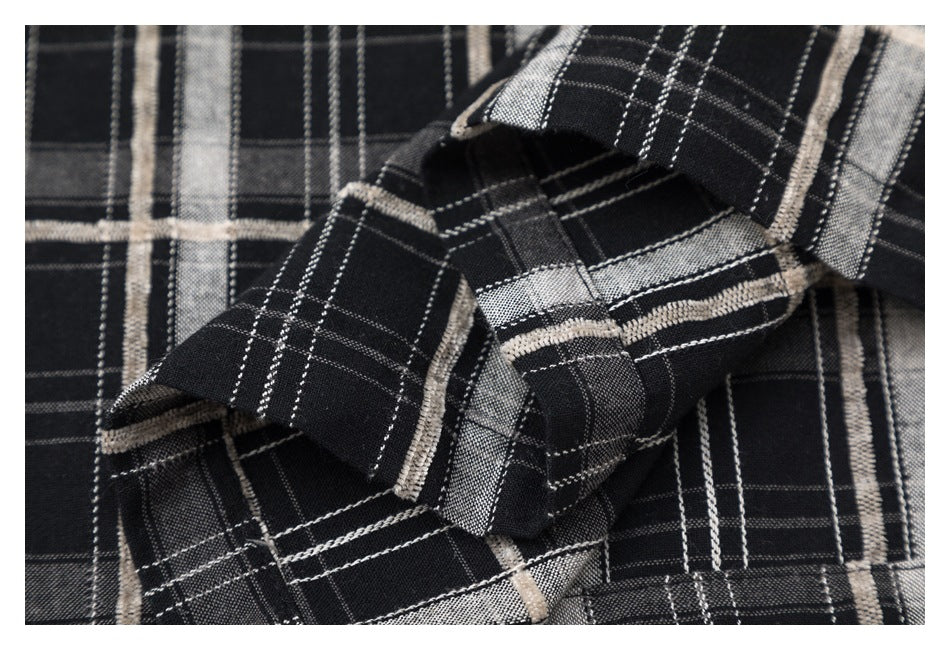 Close-up of folded black, gray, and cream plaid shirt fabric and stitching.