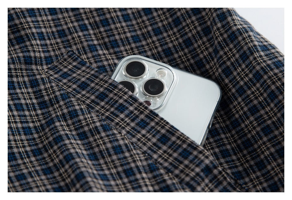Close-up of a white smartphone tucked into a pocket in dark plaid fabric with blue and beige checks.