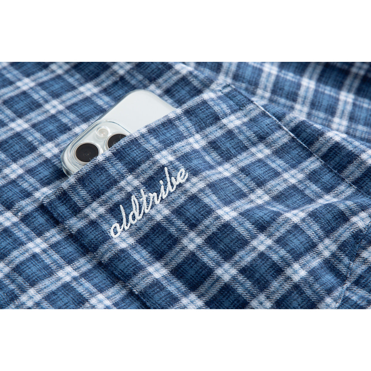 Close-up of a blue plaid shirt pocket with white script embroidery and a phone tucked inside.