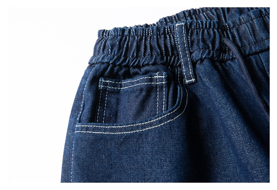 Close-up of dark indigo denim shorts showing an elastic waistband and back pocket with contrasting white stitching.