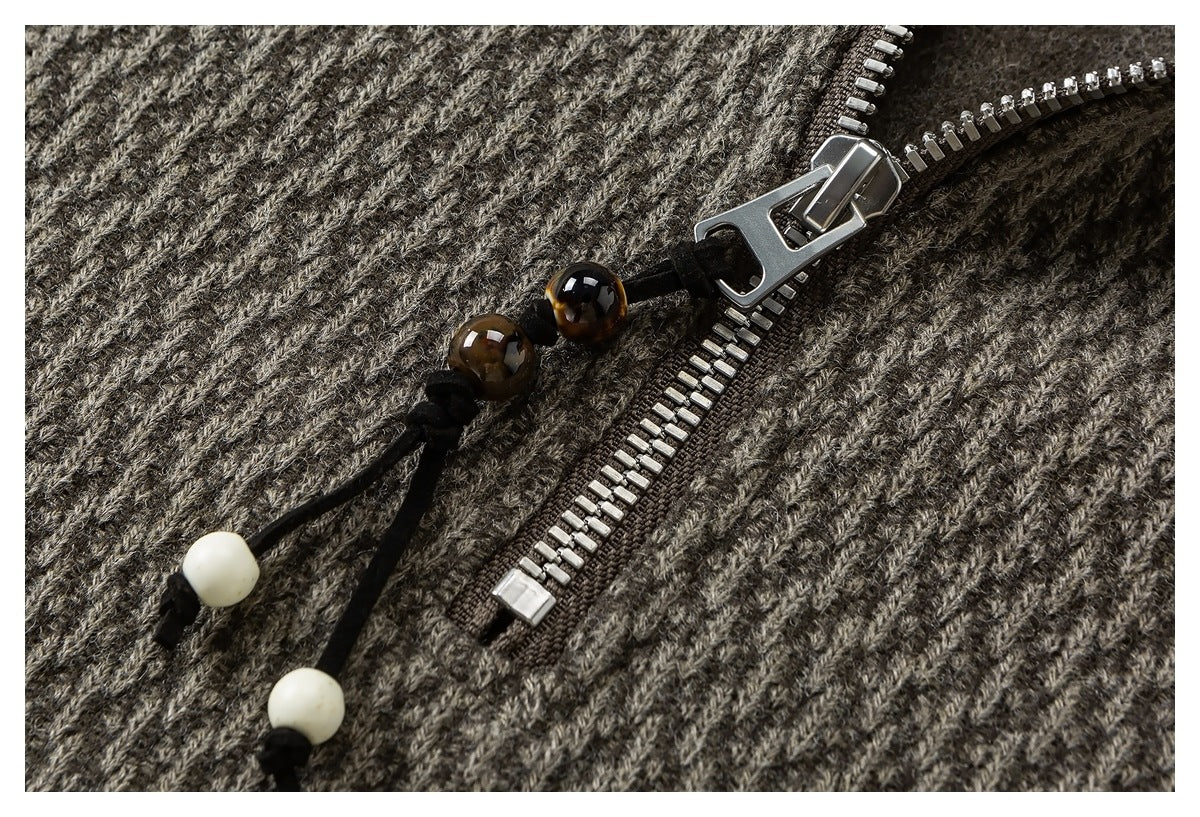 Close-up of a metal zipper with decorative bead pulls on gray-brown textured fabric.