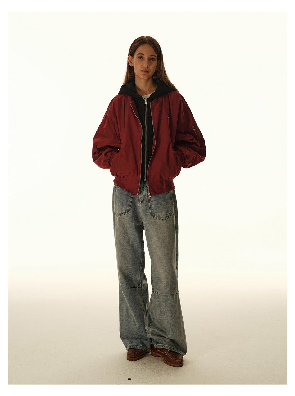Model wearing a burgundy zip-front jacket over a black hooded layer and loose gray-blue jeans.