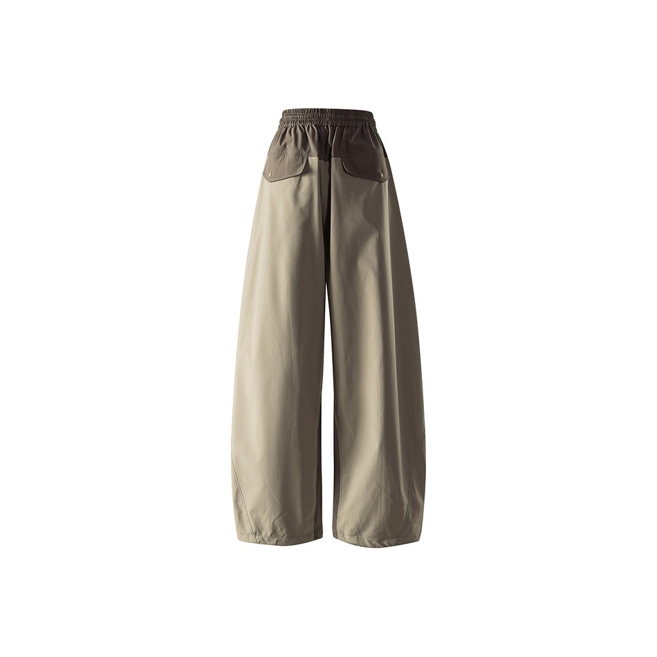 Back view of loose two-tone trousers with light khaki legs, dark brown upper panels, and flap pockets.