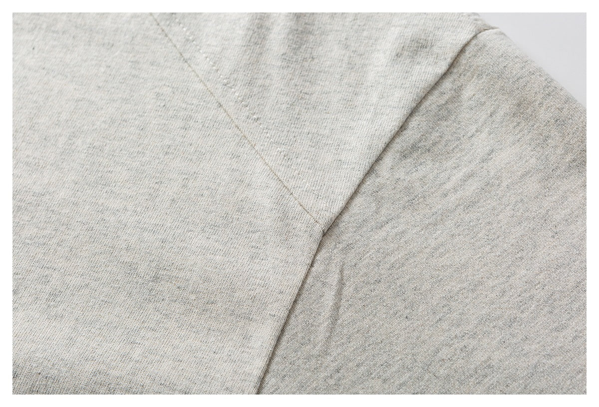 Close-up of a stitched shoulder seam on a light gray heathered garment.