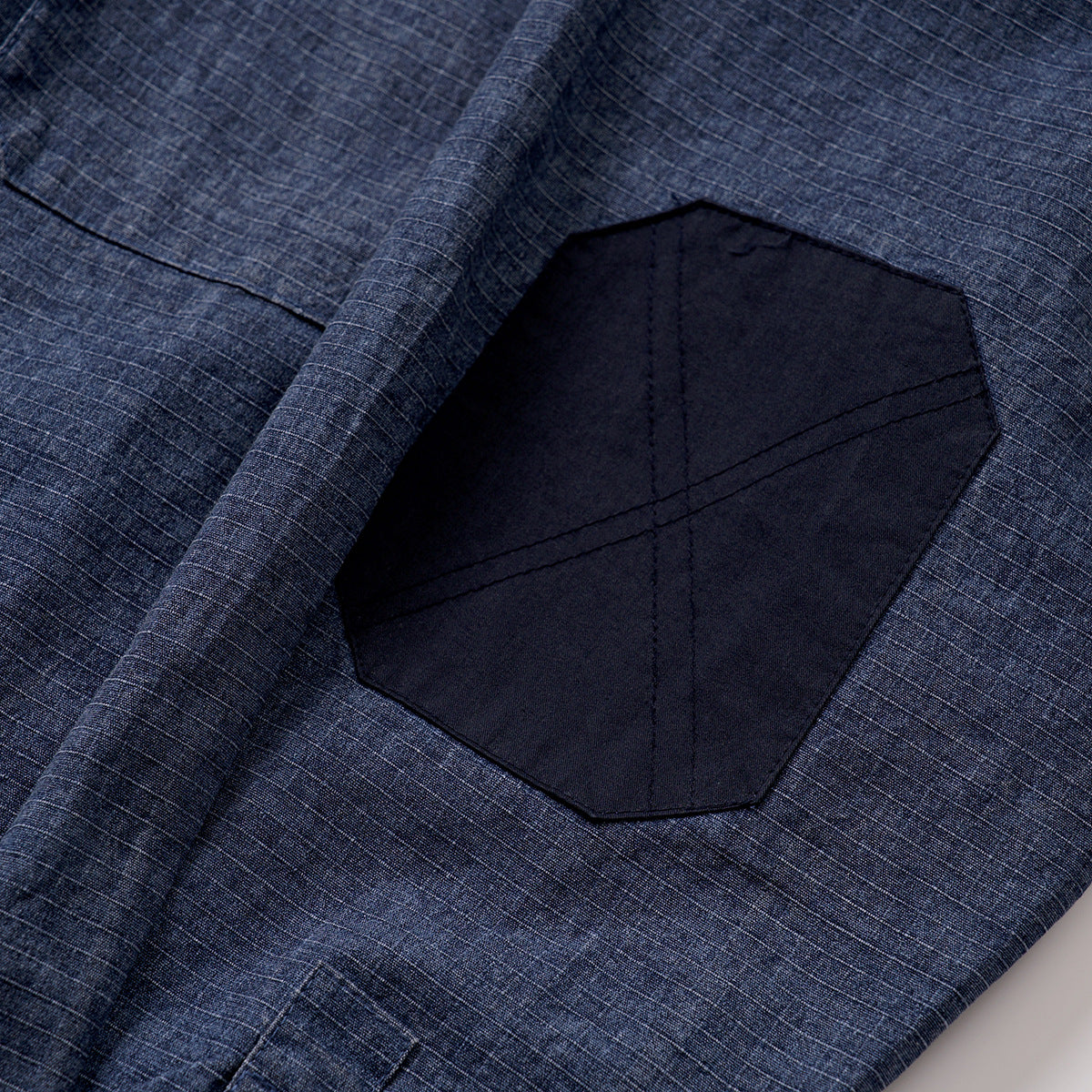 Close-up of a dark navy octagonal patch with stitching on blue grid-patterned fabric.