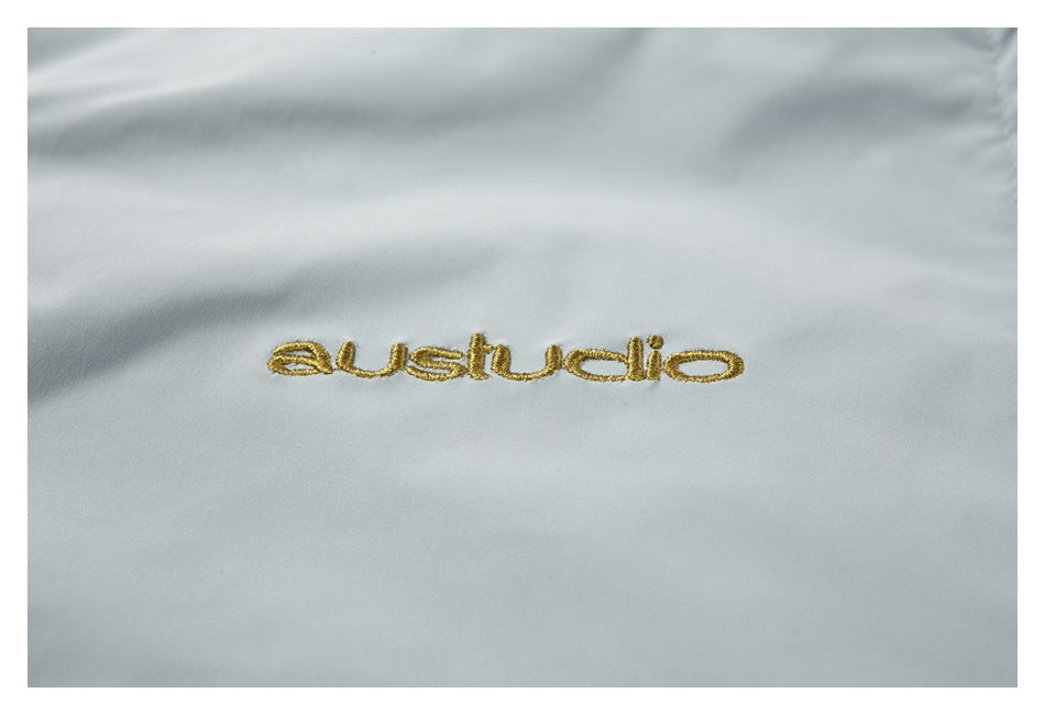 Close-up of a gold embroidered wordmark on the vest’s pale gray fabric.