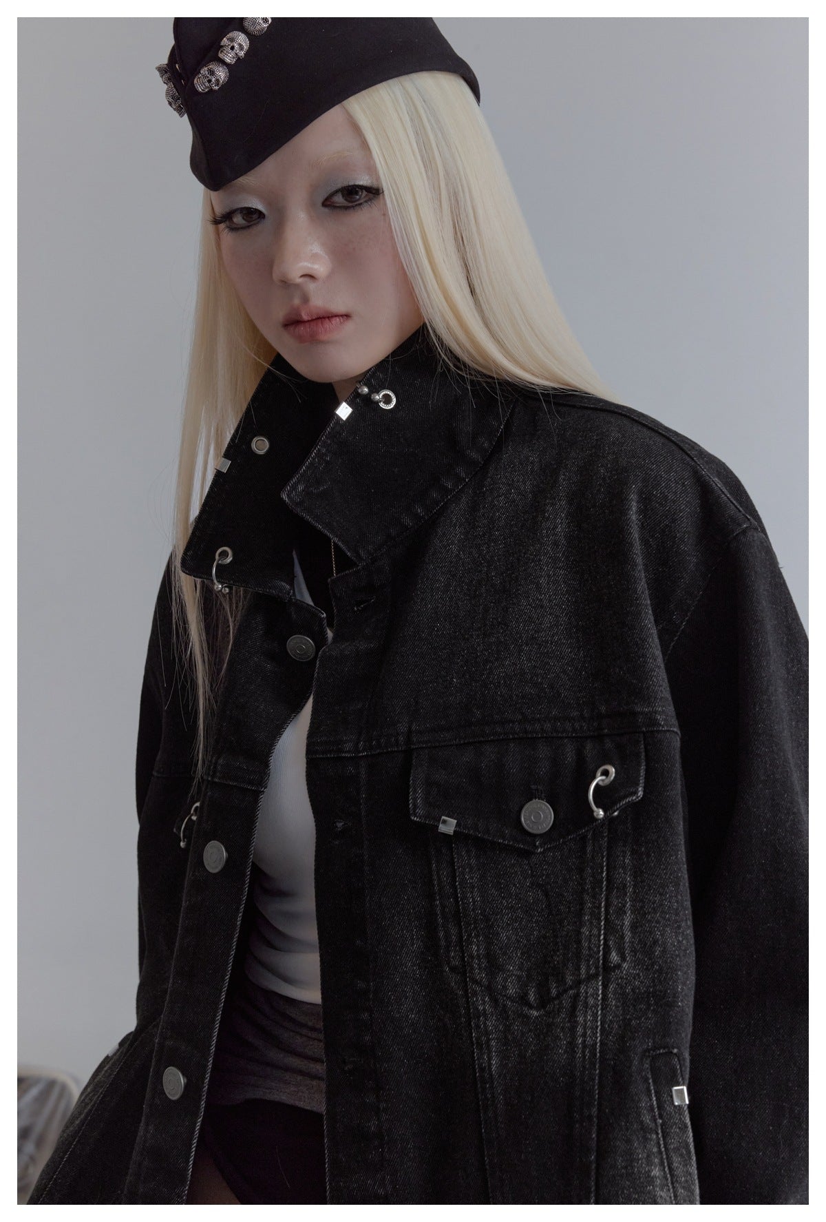 Close-up of a model wearing the black denim jacket, highlighting its high collar, chest pocket, and metal details.