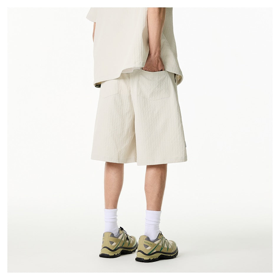 Rear view of a model wearing ivory shorts with two back pockets and a matching short-sleeve shirt.