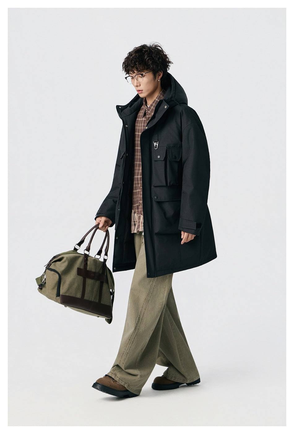 Model walking in a long black hooded parka with flap pockets and a snap-front closure.