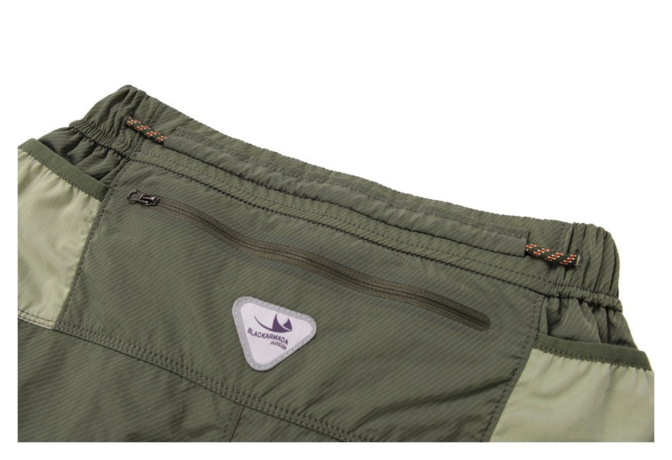 Close-up of the olive shorts' rear waistband, zip pocket, brand patch, and pale contrast side panels.