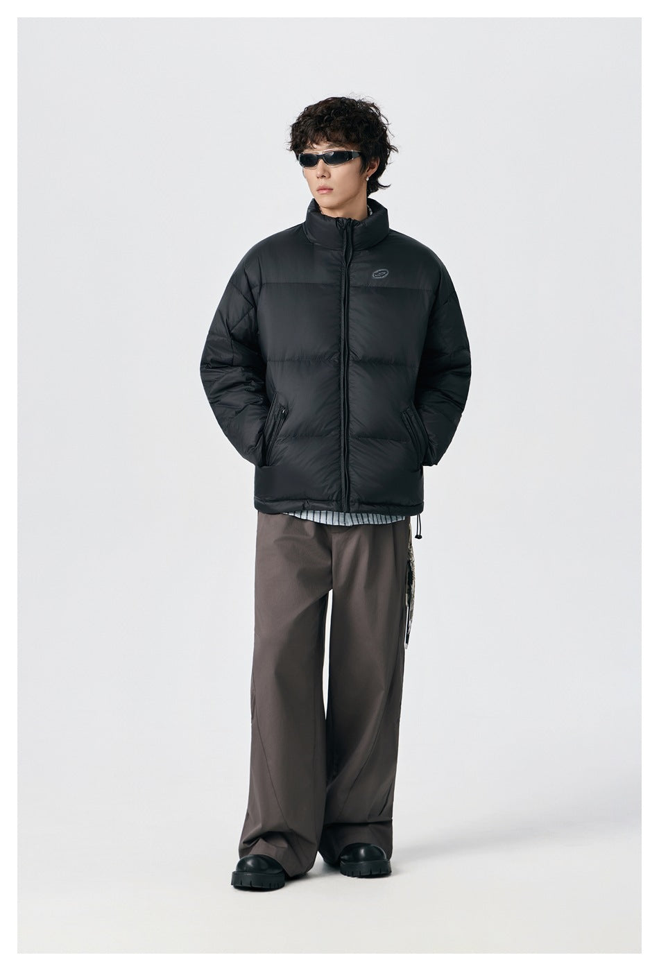 Model wearing black puffer jacket zipped up over a striped shirt with brown wide-leg pants and chunky black shoes