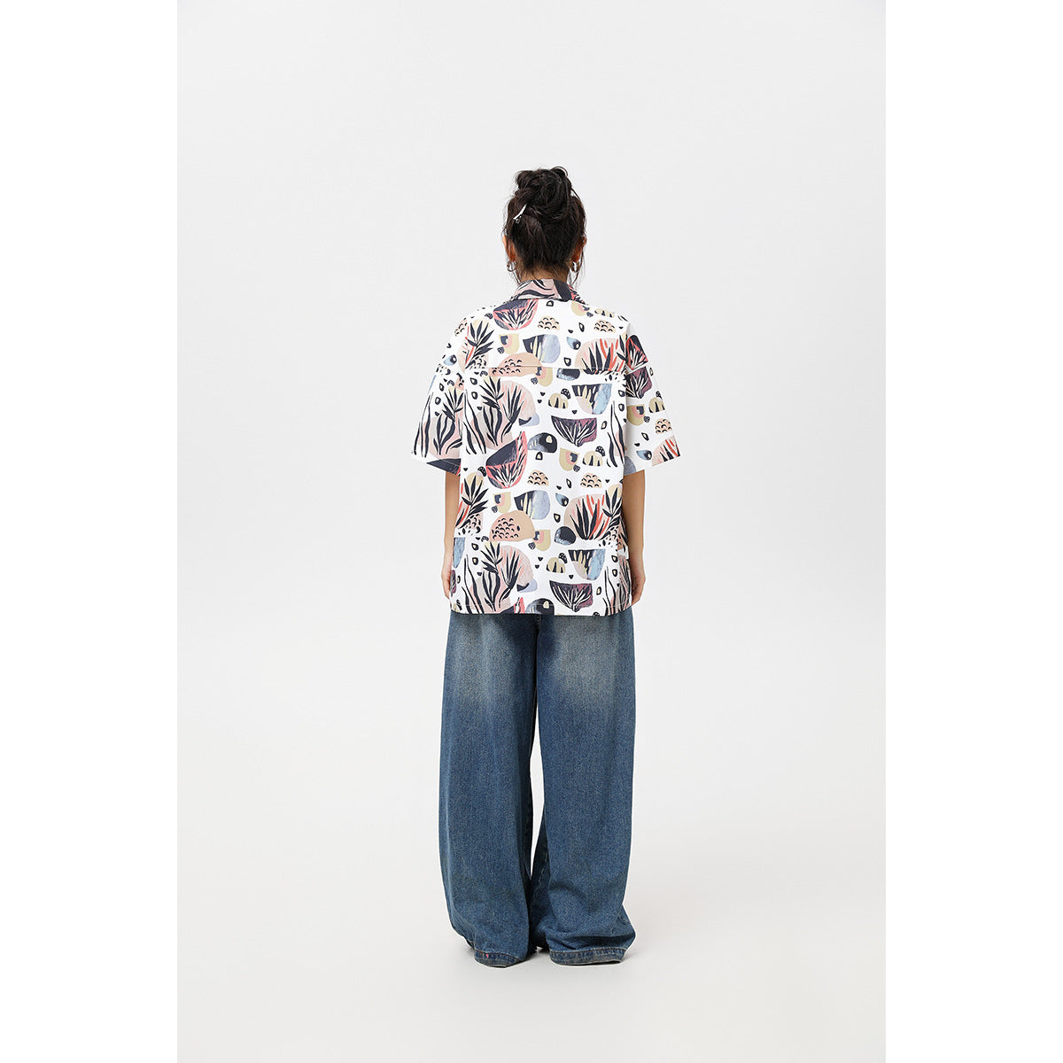 Back view of a model wearing a white abstract botanical-print short-sleeve shirt with wide-leg blue jeans.