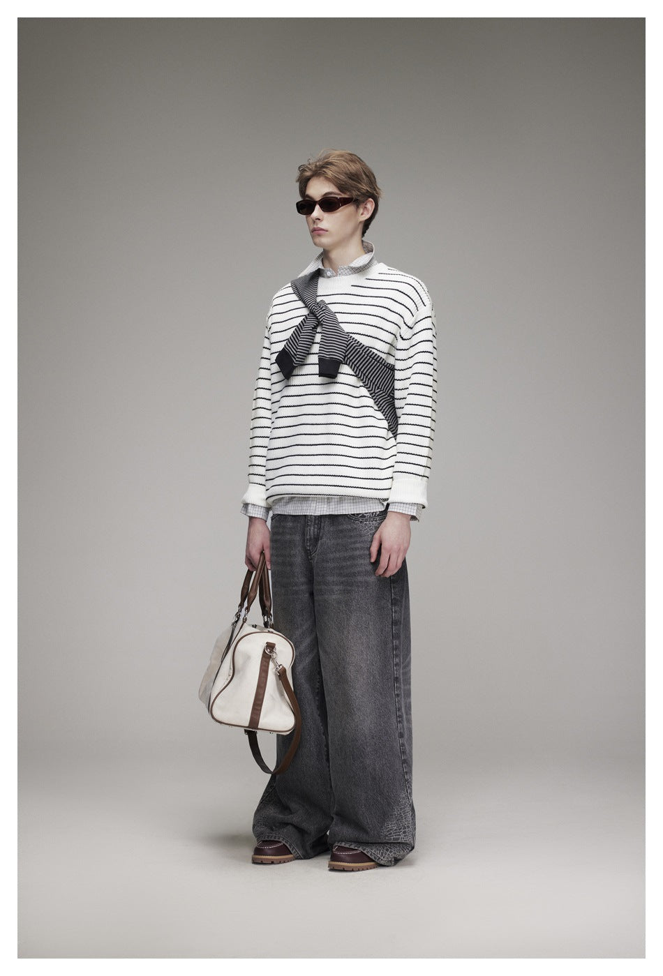 Front view of a model in a white sweater with thin black stripes and a dark striped knit draped across the chest.