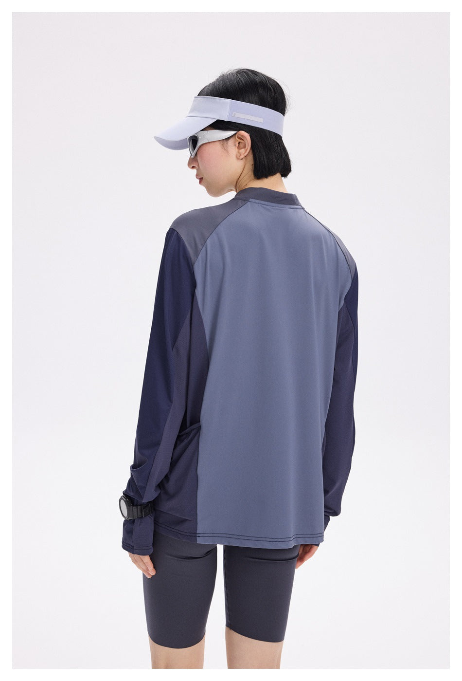 Back view of a model wearing a slate-blue and navy color-block long-sleeve top with dark shorts.
