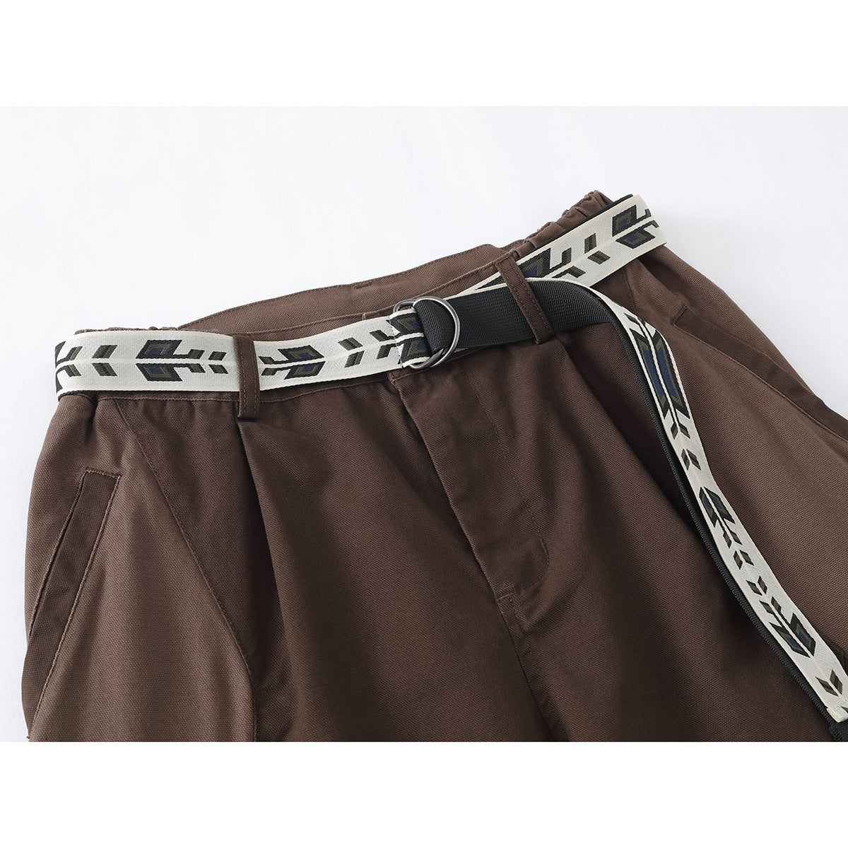Close-up of brown trousers with pleats, a patterned cream belt, black strap and metal ring buckle.