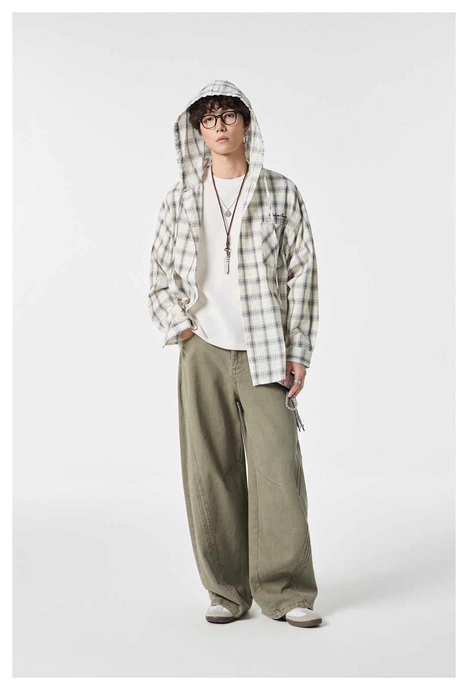 Model wearing open cream plaid hooded shirt over white tee with olive wide-leg pants, front view