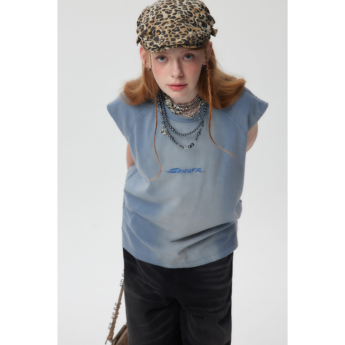 Front view of a model in a loose slate-blue sleeveless top with blue chest embroidery and black trousers.