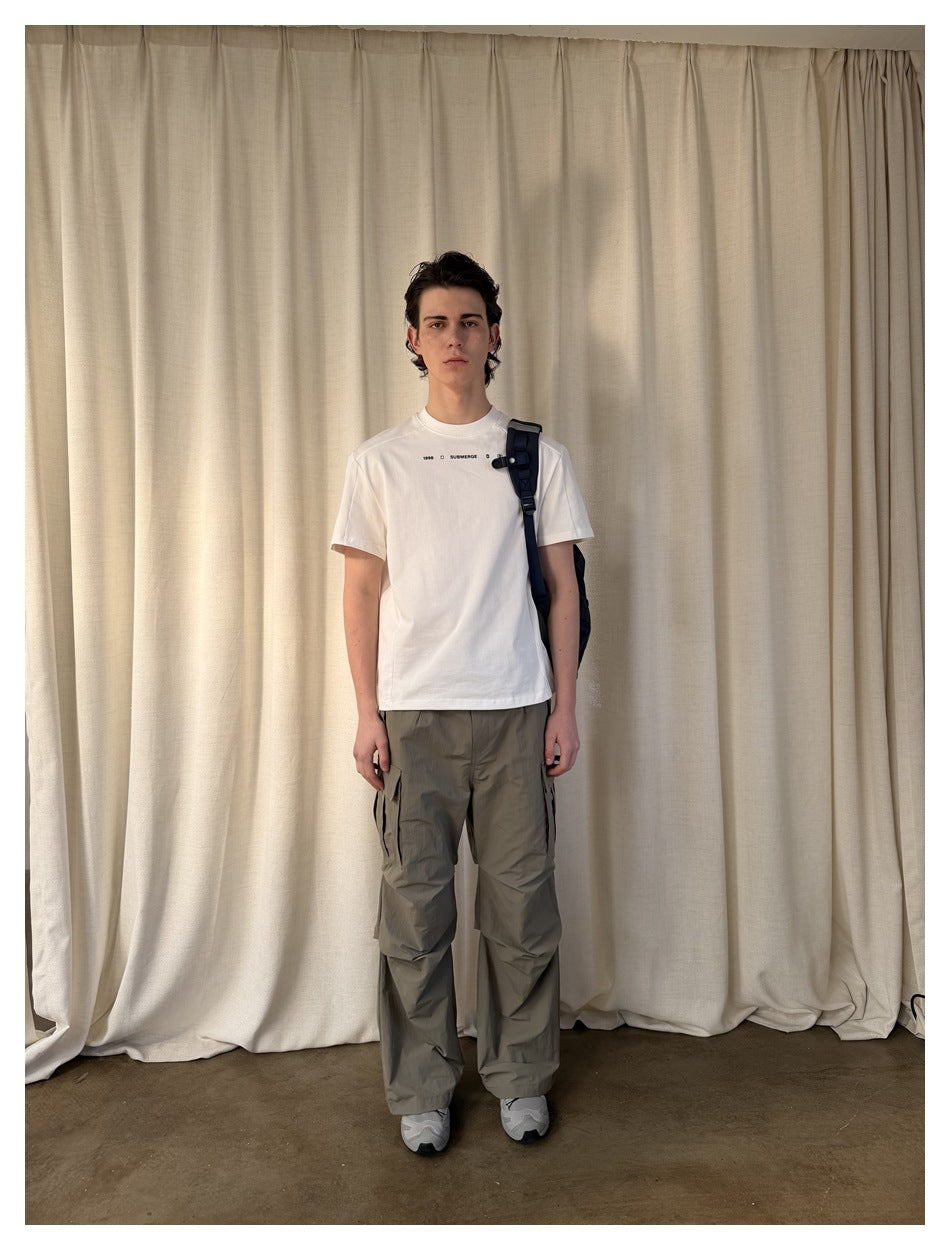 Model in white short-sleeve T-shirt with chest print, olive cargo pants and a navy shoulder bag, front view